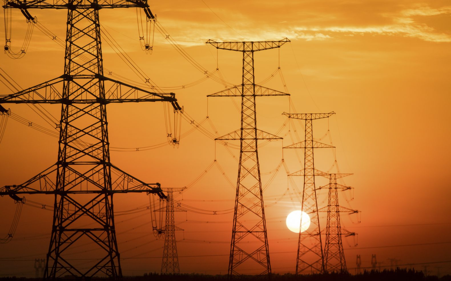 Black silhouette of rows of power lines with sun setting and an orange sky in the background.