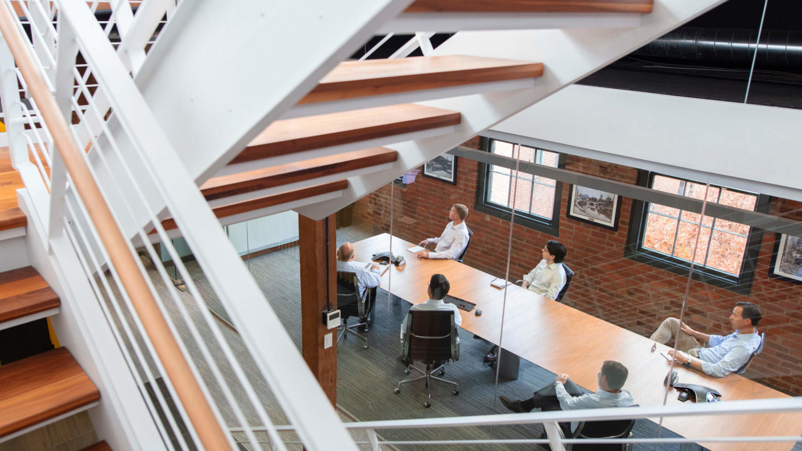 employees sitting at a conference room table seen through staircase above