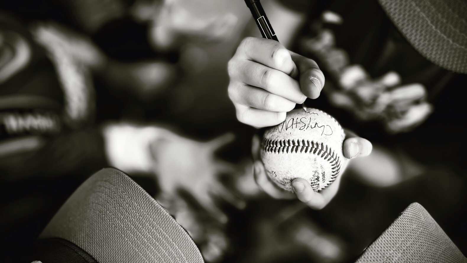 person wearing hat signing baseball in black and white