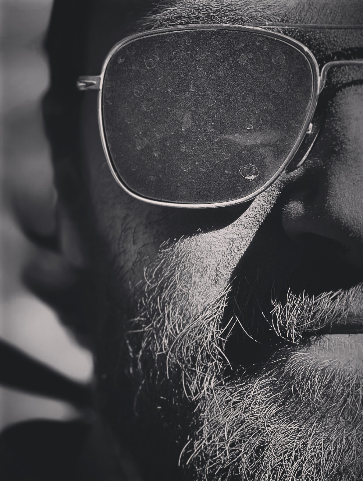 half of bearded man’s face wearing sunglasses caked with light dirt spots