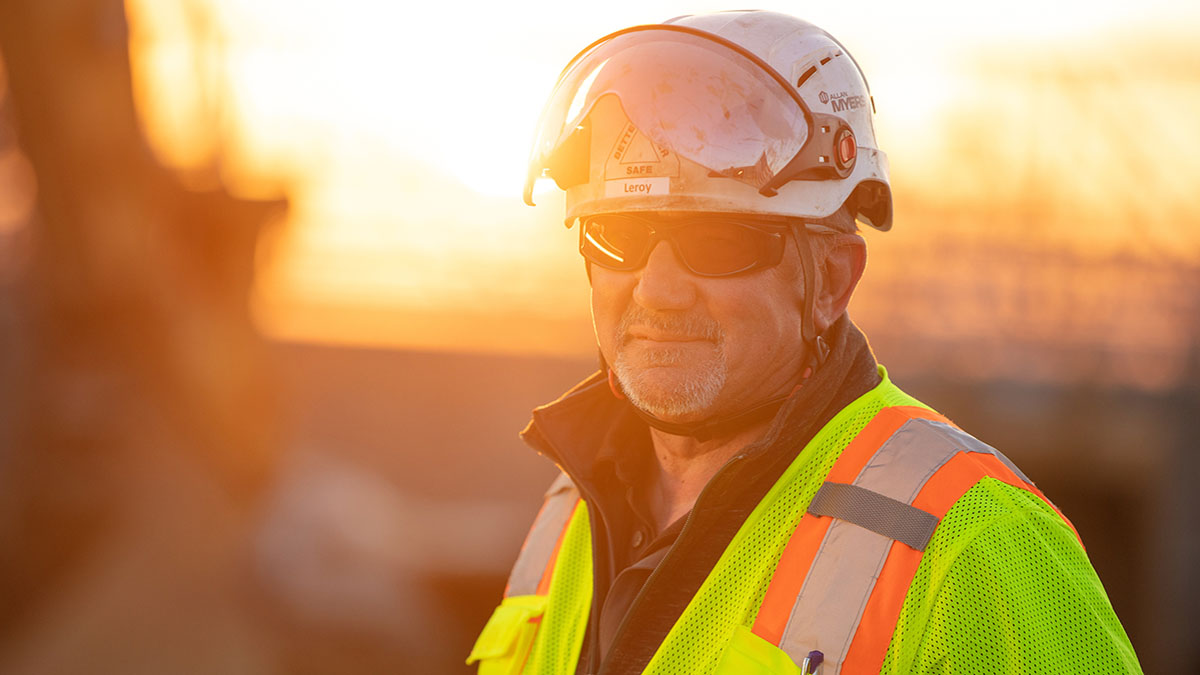 male construction worker wearing neon yellow and orange vest with helmet and eye protection