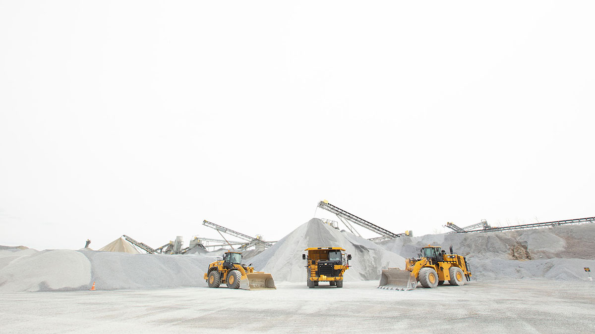 Three construction vehicles parked on site in front of pile of stones