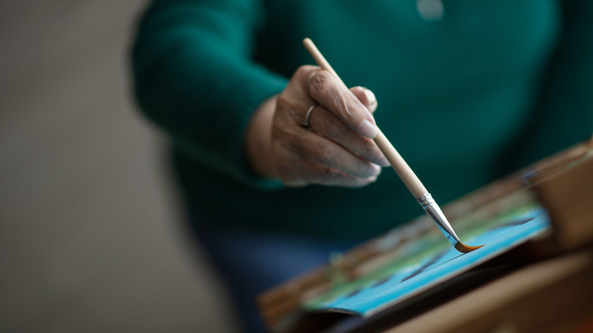 Close up of older woman painting with wooden paintbrush