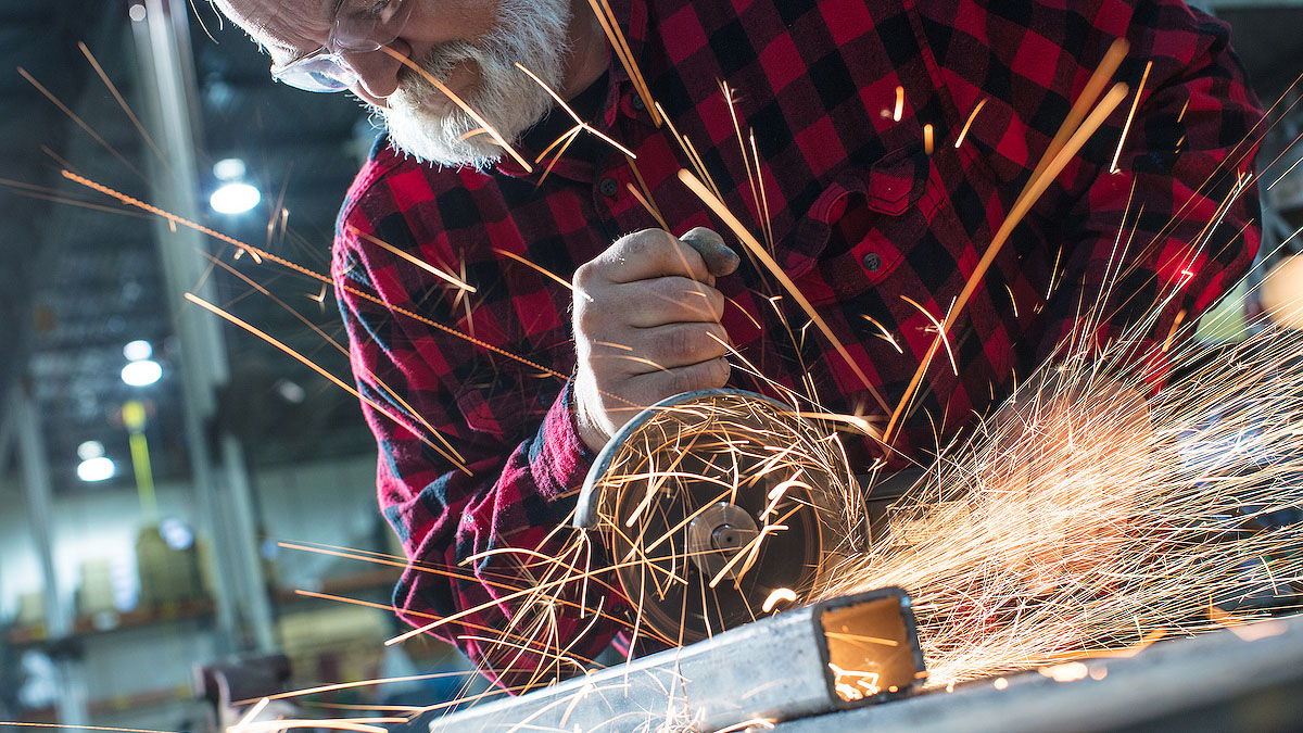 man with beard in flannel using hand saw to cut metal with sparks flying