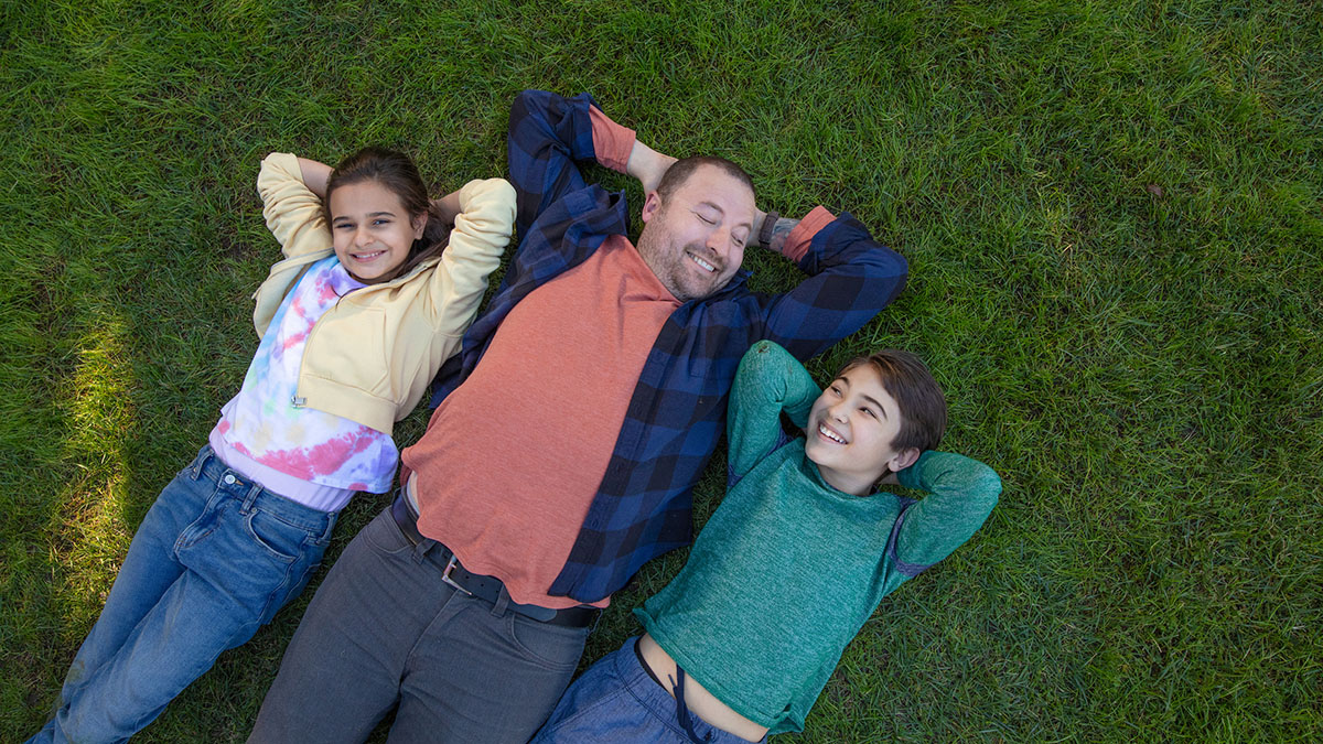 Man laying in grass next to kids with hands behind heads