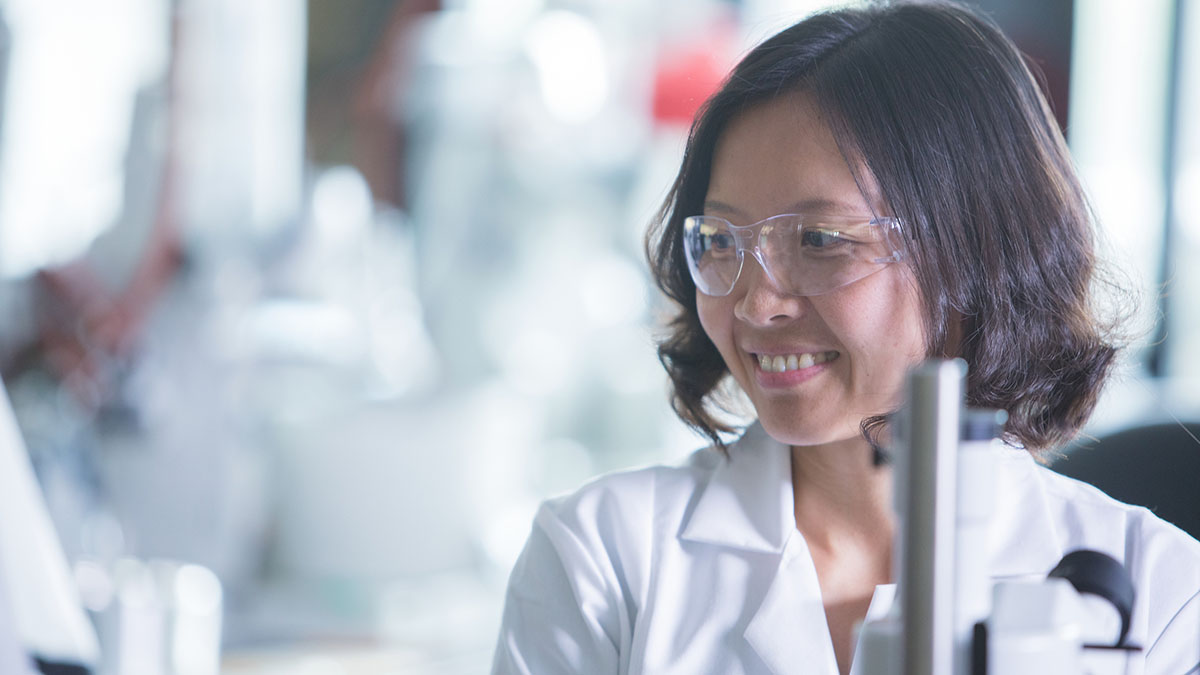 Woman with protective glasses and lab coat smiling