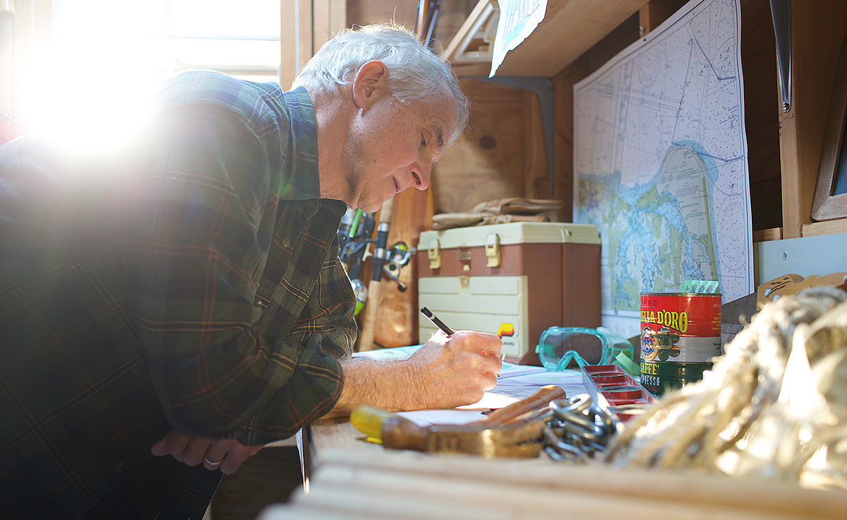 man with white hair at work bench writing with pen