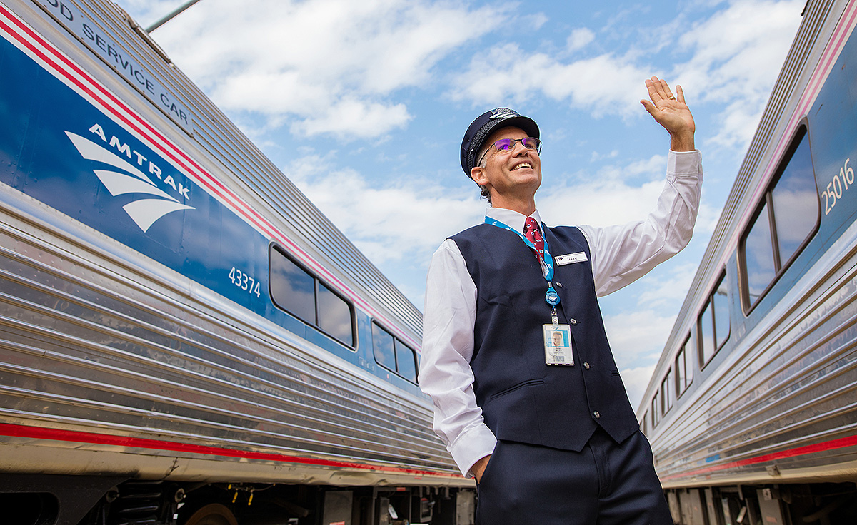 Amtrak employee in uniform waving at train car