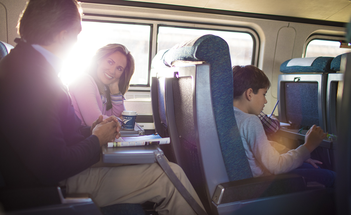 Female and male adult talking on Amtrak train with male child sitting in front of them