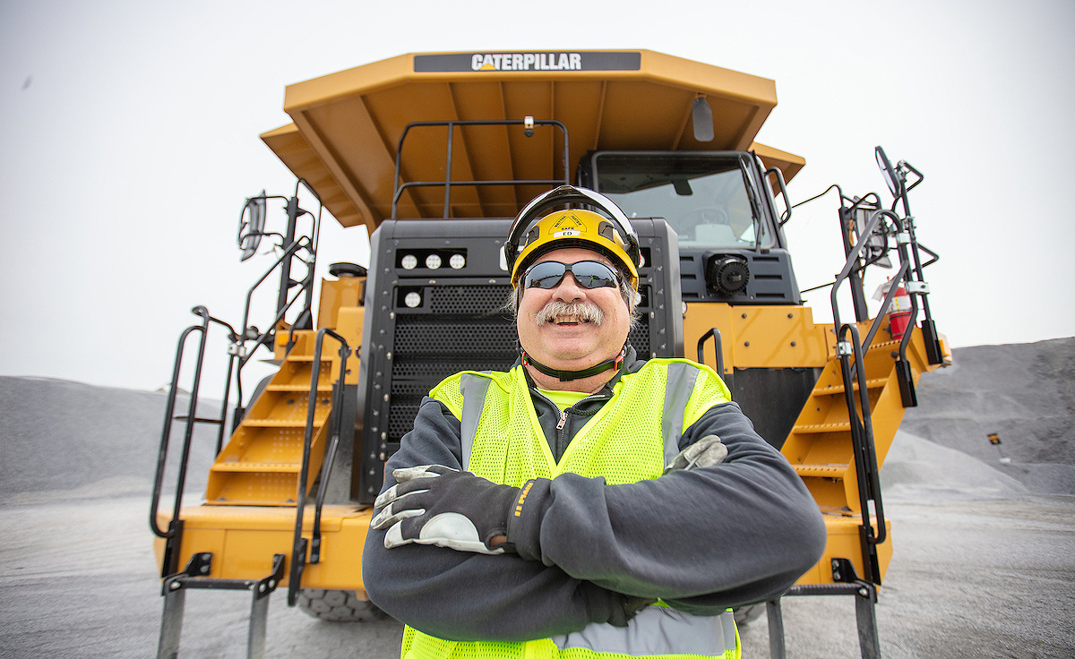 Construction worker standing in front of Caterpillar machine smiling