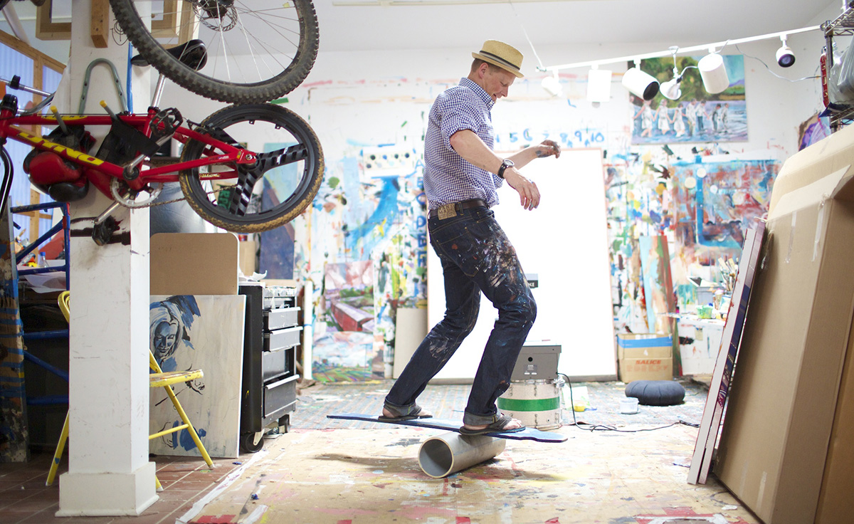 Male artist in studio riding a board on top of a tube-shaped object