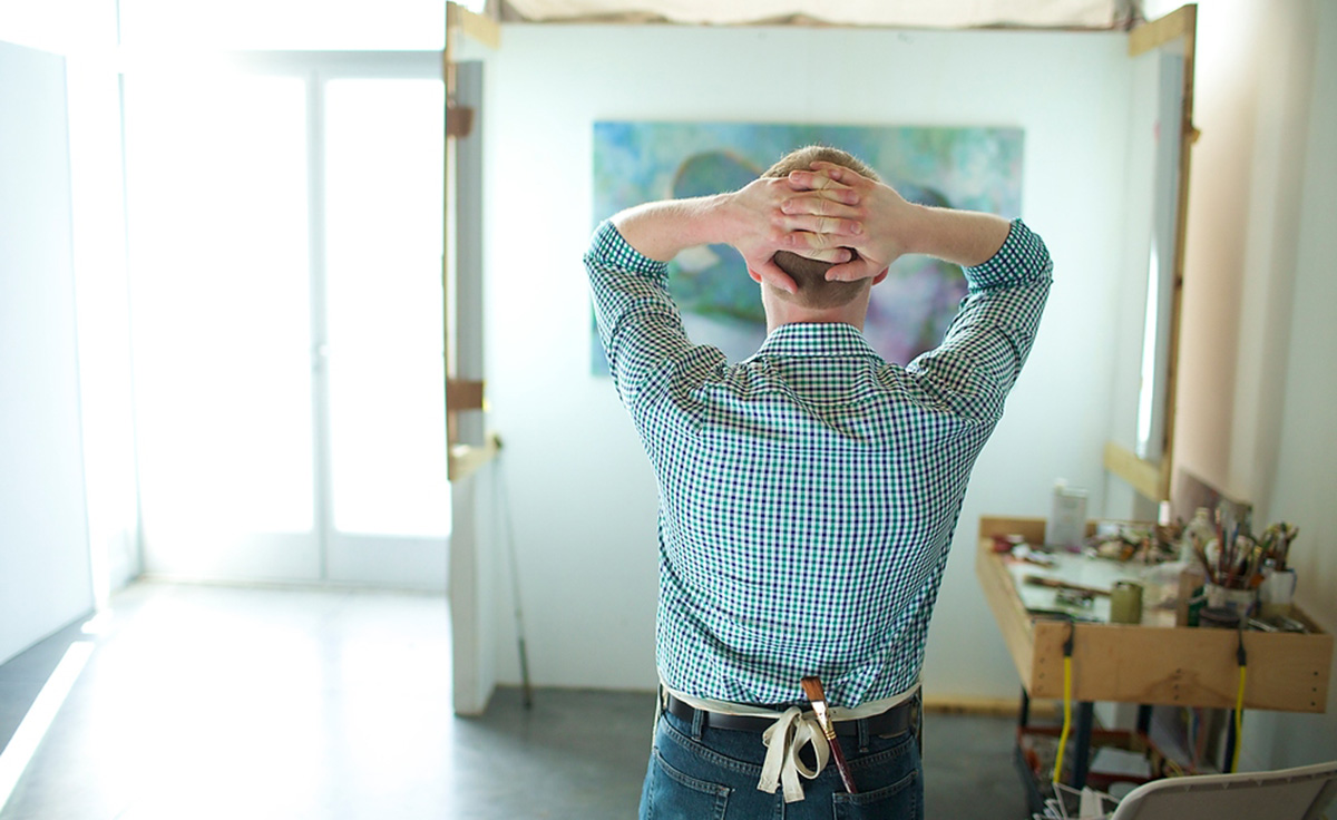 male artist with hands over head looking at completed work