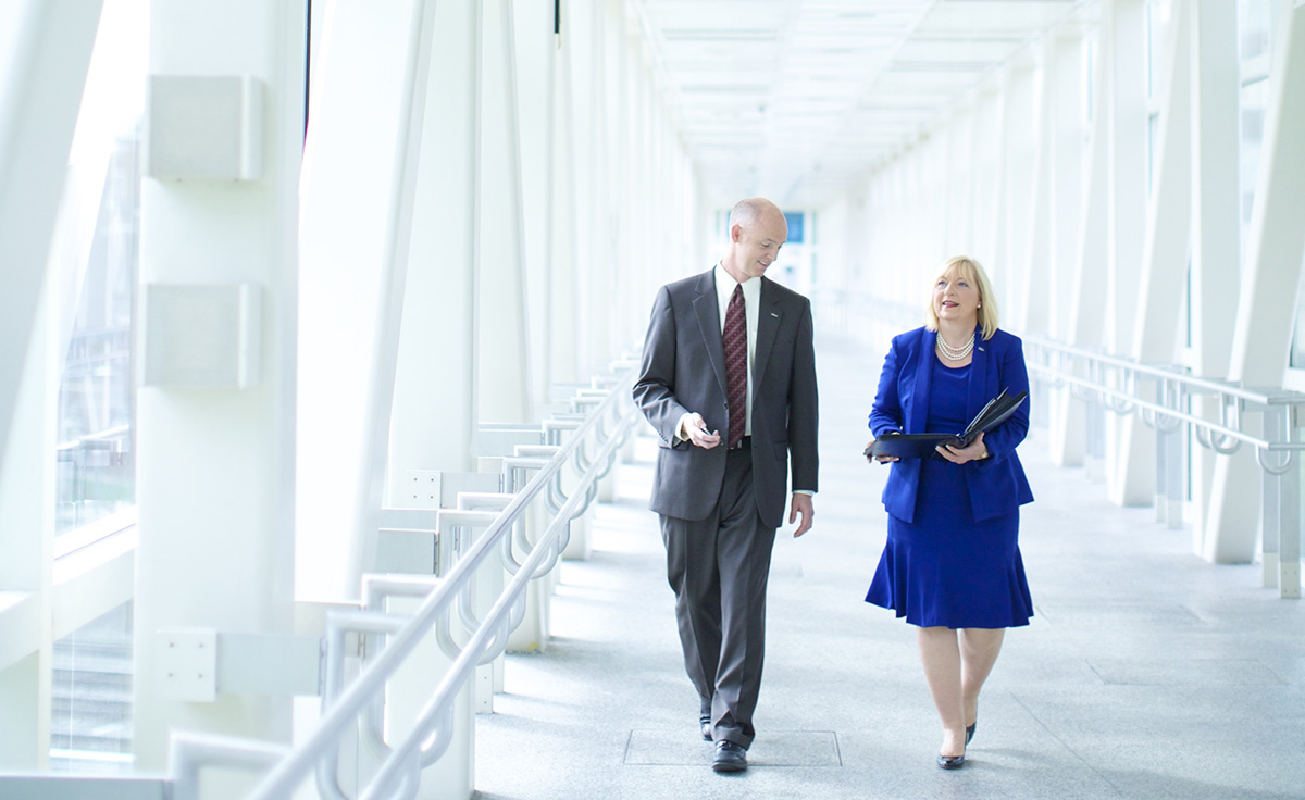 two commercial corporate employees walking through bright naturally lit white hallway