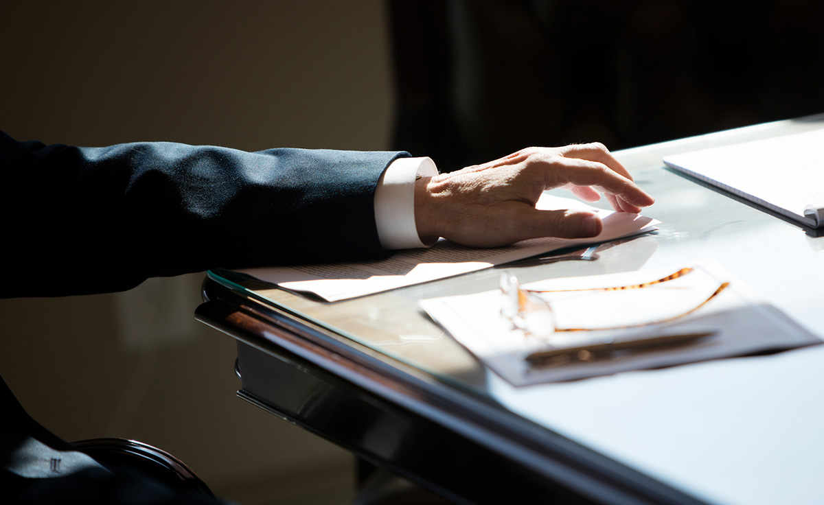 hand with vein resting on piece of paper on desk wearing suit and dress shirt