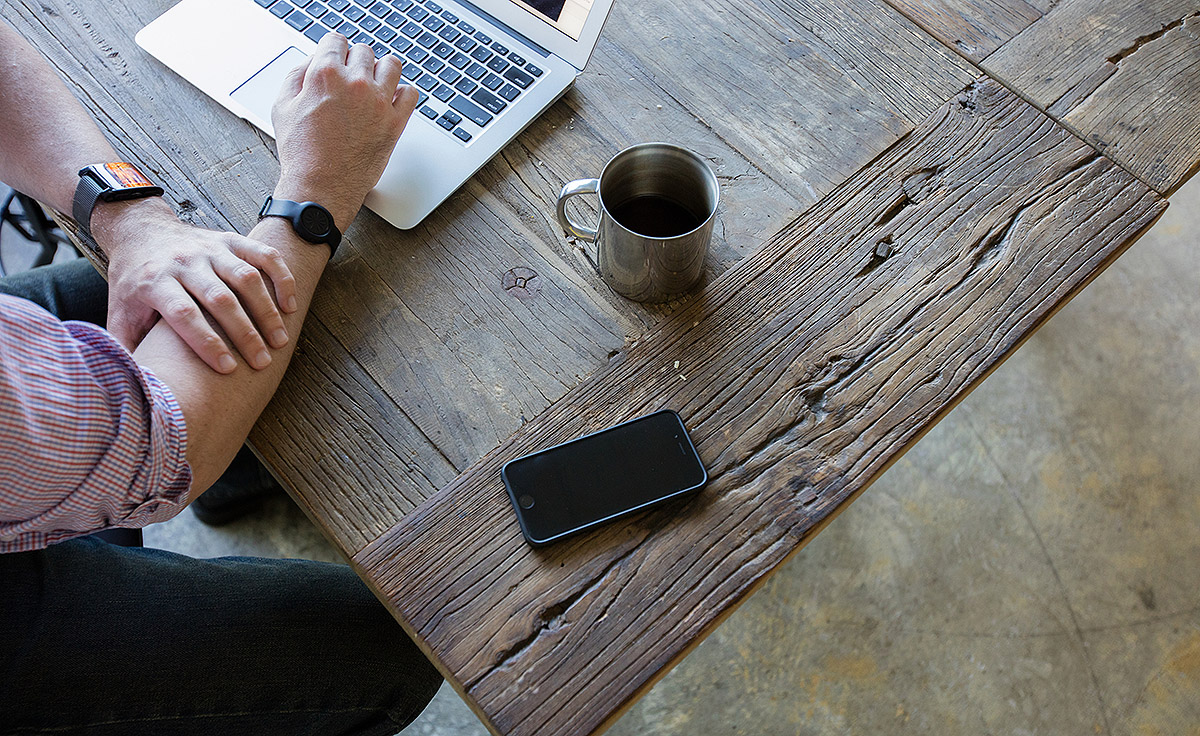 individual working at wooden table with macbook iphone and coffee mug