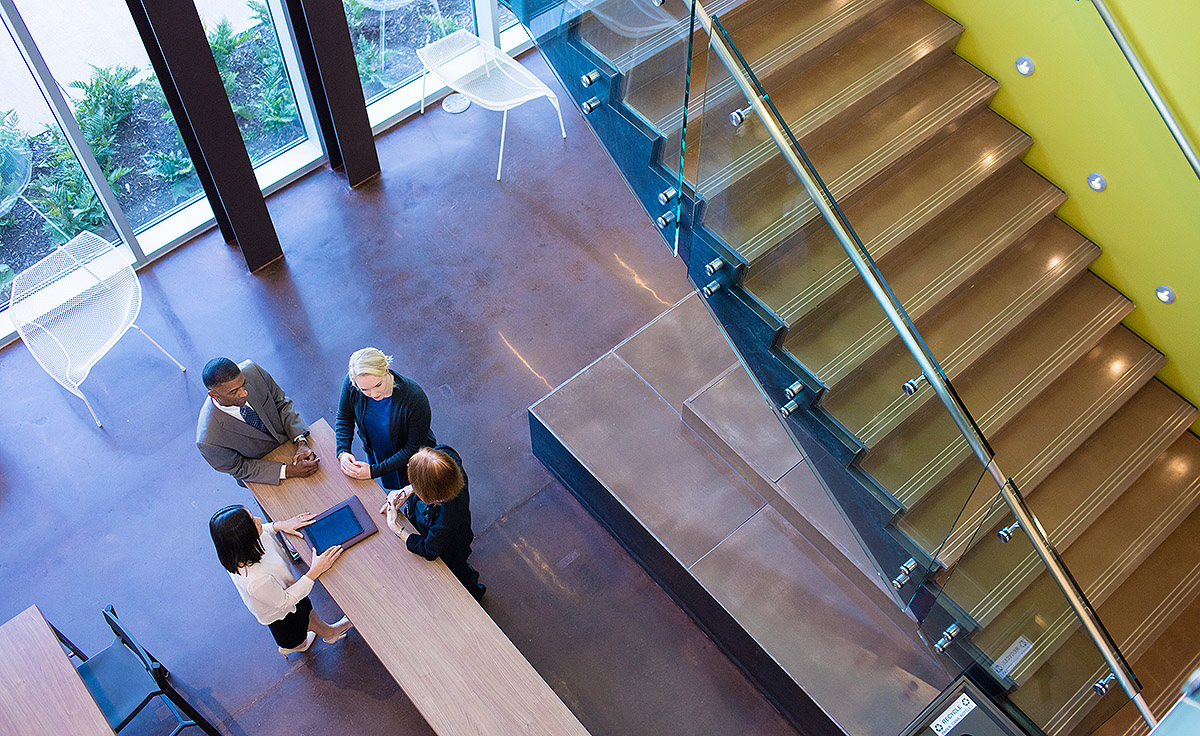 four employees standing at rectangle wooden table with stairs to the right