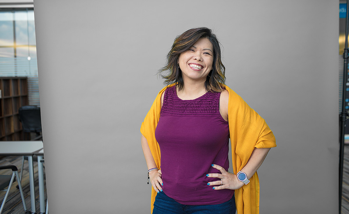 female with purple tank top and yellow throw smiling with gray background