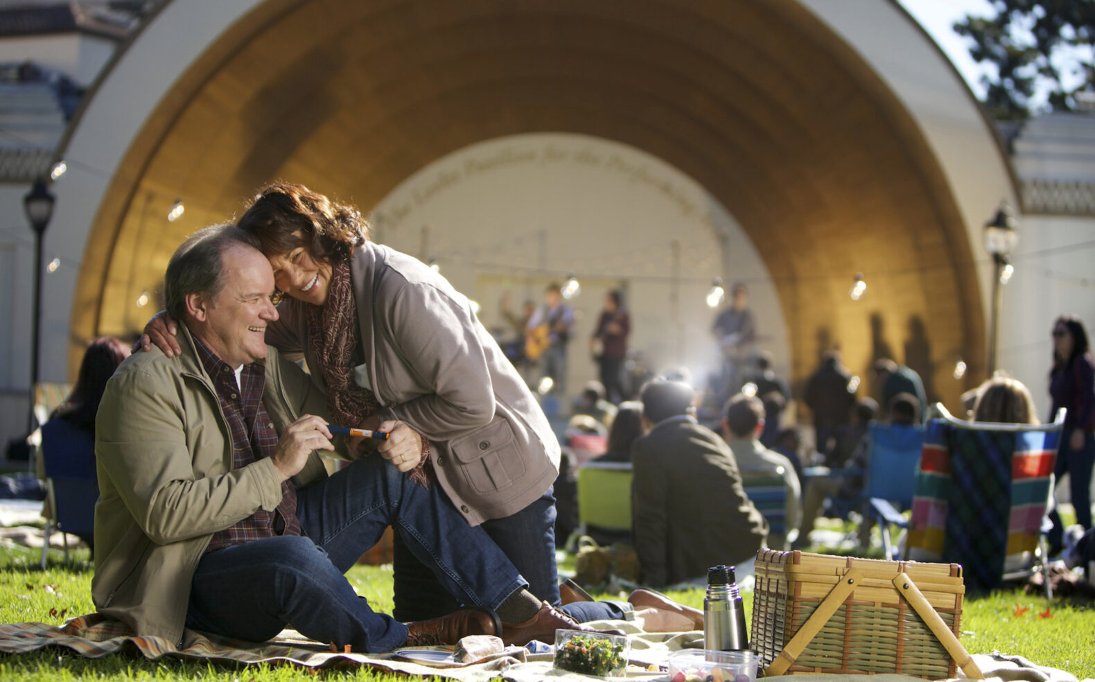 couple sitting at park laughing during concert at amphitheater pavilion