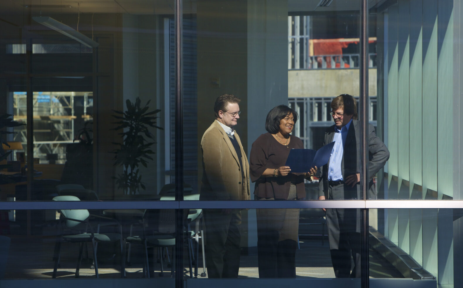 three coworkers discussing and looking at folder in office through window