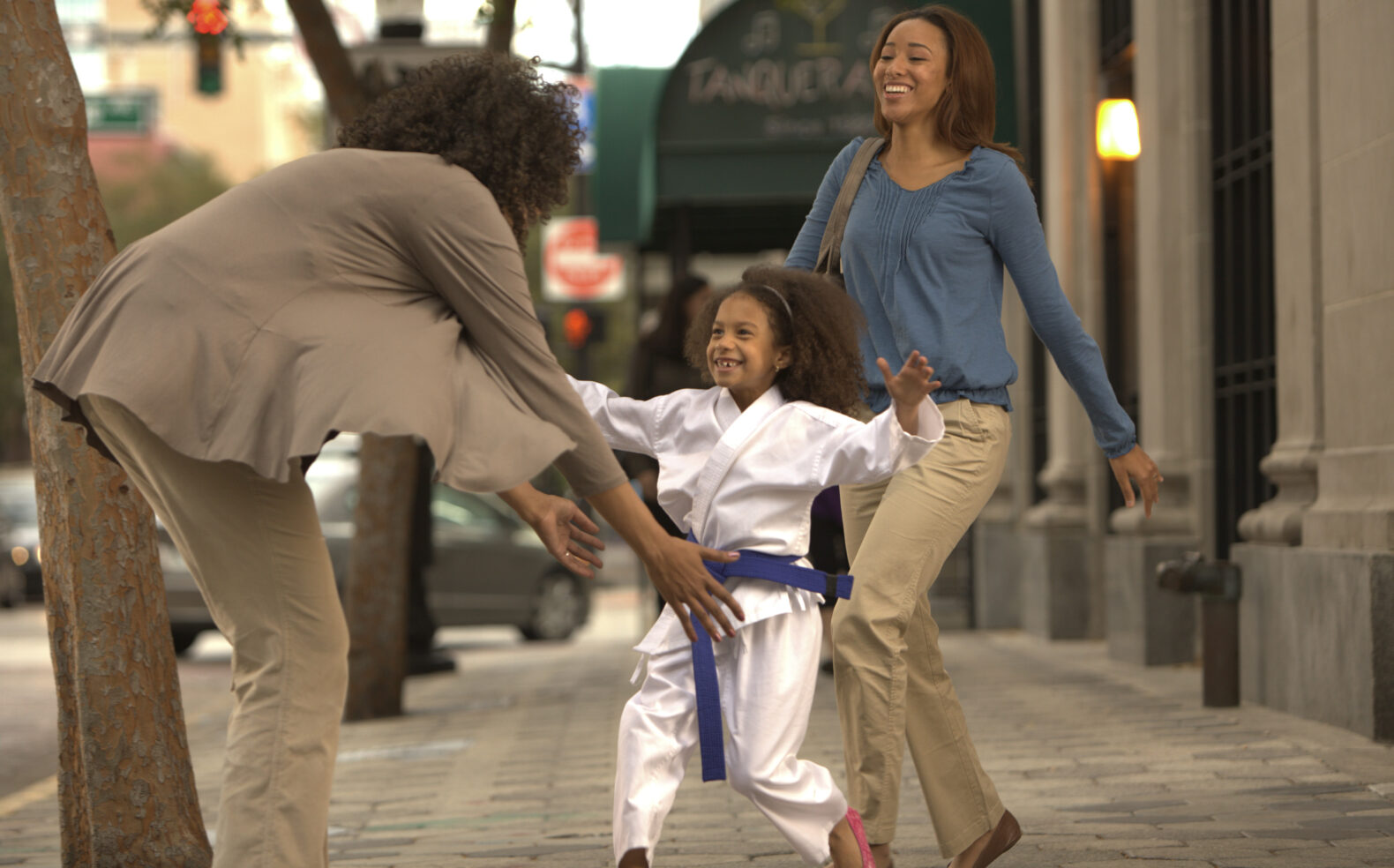 young girl in karate outfit runs to hug lady in brown outfit